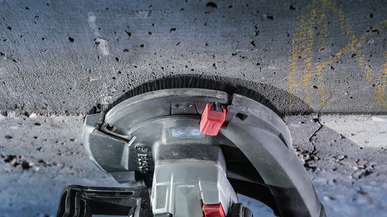 콘크리트 표면을 따라 연삭하는 전동 공구, 먼지 브러시 부착물이 보입니다.