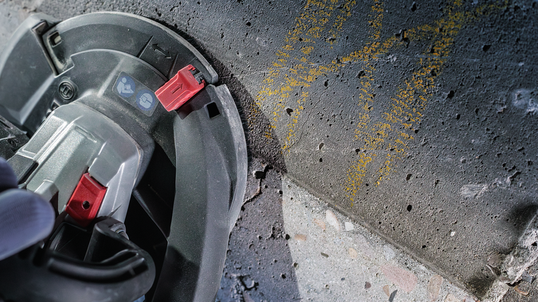 안전 장비를 착용한 사람이 원형 톱을 사용하여 콘크리트 표면을 자릅니다.