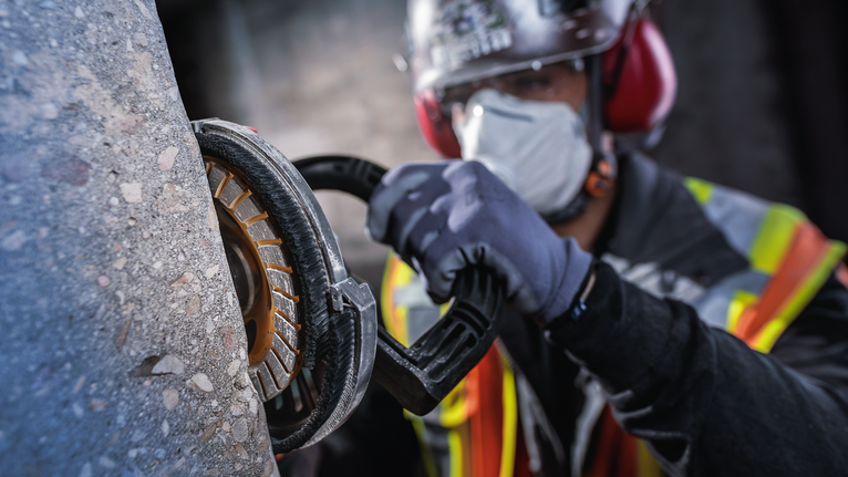 안전 장비를 착용한 사람이 전동 공구로 콘크리트를 갈아내고 있습니다.