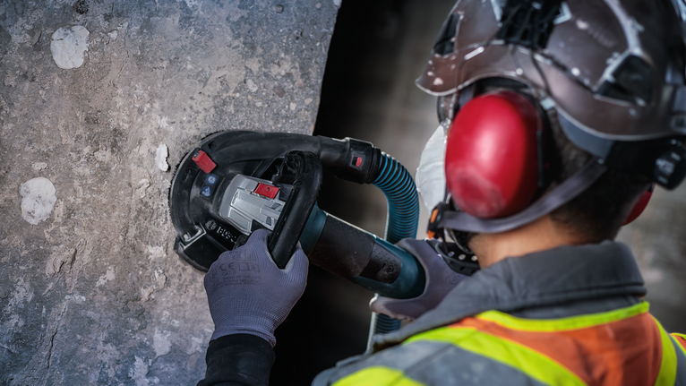 안전 장비를 착용한 사람이 전동 공구로 콘크리트 벽을 갈아내고 있습니다.