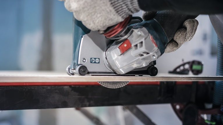 안전 장비를 착용한 사람이 전동 공구를 작동하여 타일을 자르고 있습니다.