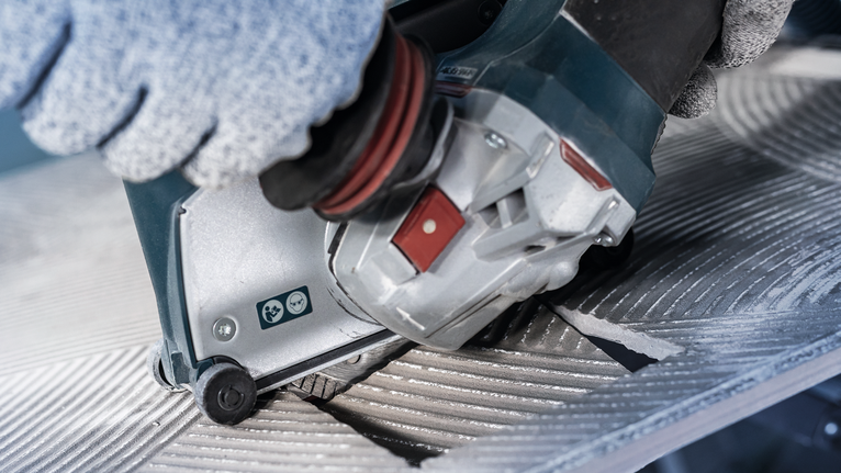 안전 장비를 착용한 사람이 전동 공구를 작동하여 홈이 있는 금속 표면을 절단합니다.