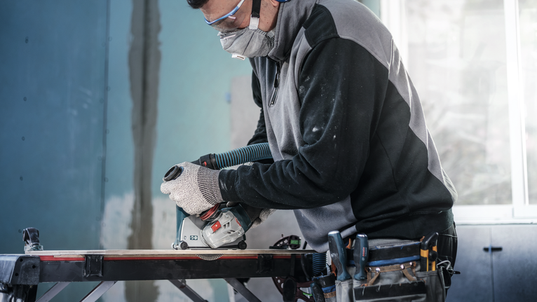 안전 장비를 착용한 사람이 작업대에서 원형 톱을 사용하여 나무를 자르고 있습니다.