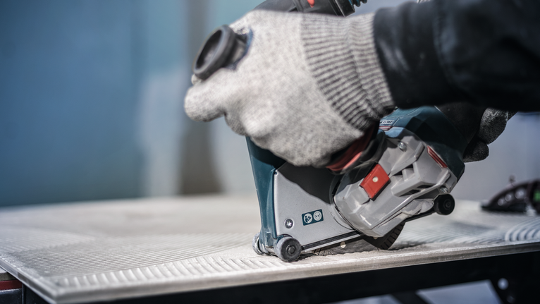 안전 장비를 착용한 사람이 전동 공구를 사용하여 타일을 자르고 있습니다.