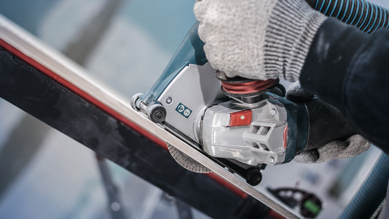 안전 장비를 착용한 사람이 전동 공구를 사용하여 금속 막대를 자릅니다.