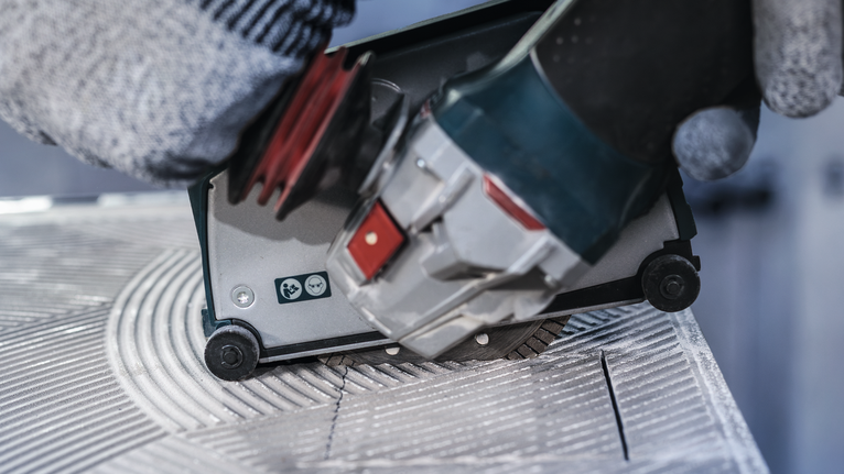 안전 장비를 착용한 사람이 전동 공구를 조종해 타일에 홈을 파고 있습니다.