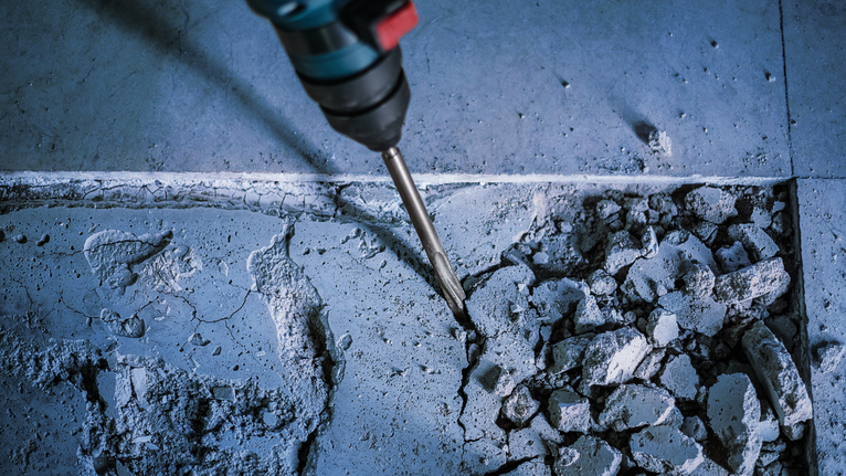 회전 망치로 콘크리트 바닥 타일을 부수고 있습니다.