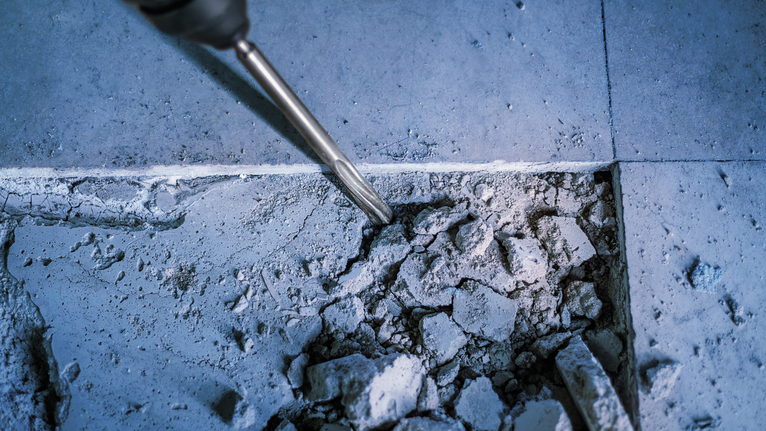 회전 해머 끌로 콘크리트 바닥을 부수는 모습입니다.