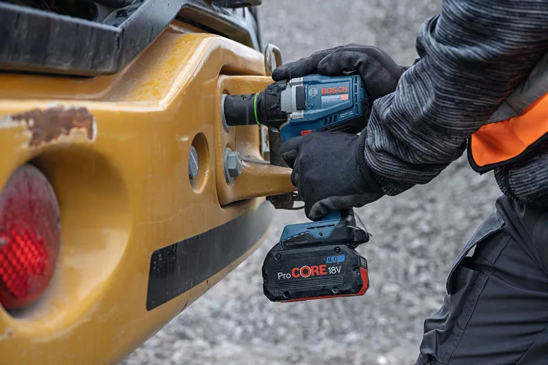 안전 장비를 착용한 사람이 중장비에 무선 충격 렌치를 사용하고 있습니다.