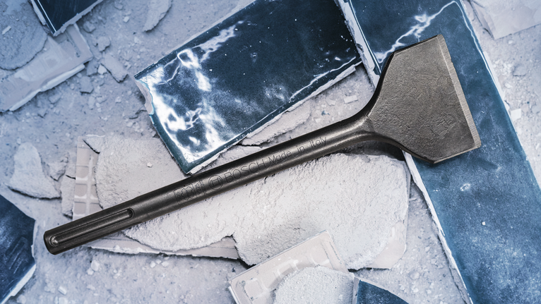 먼지가 덮인 깨진 콘크리트 바닥 위에 넓은 끌이 놓여 있다.