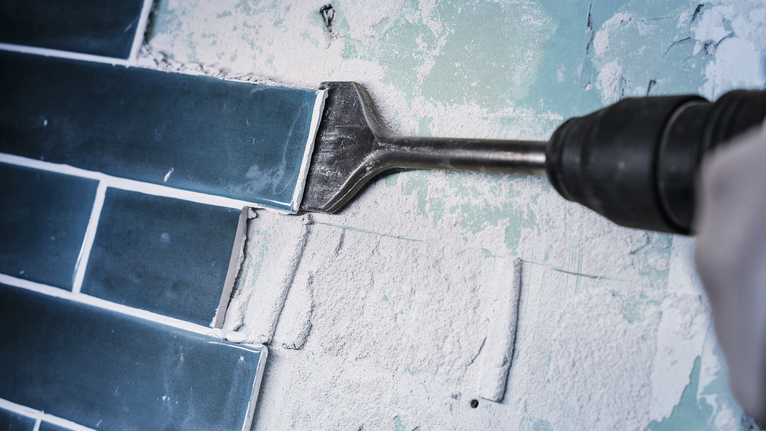 끌 부착물이 달린 전동 공구로 벽 타일을 제거합니다.