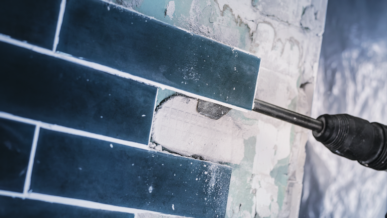 전동 공구로 벽에서 푸른 타일을 떼어내고 있습니다.