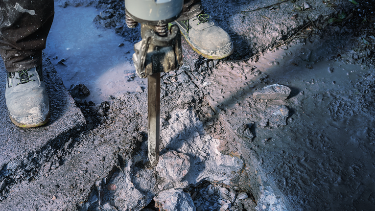 안전 장비를 착용한 사람이 철거 망치로 콘크리트를 부수는 모습.