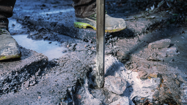 안전 장비를 착용한 사람이 철거 도구를 사용하여 야외에서 콘크리트를 깨고 있습니다.