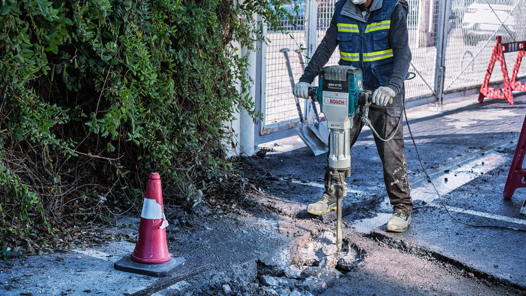 안전장비를 착용한 사람이 철거도구를 이용해 콘크리트를 깨고 있습니다.