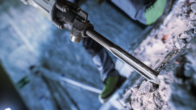 안전 장비를 착용한 사람이 철거 망치를 사용하여 콘크리트를 깨고 있습니다.