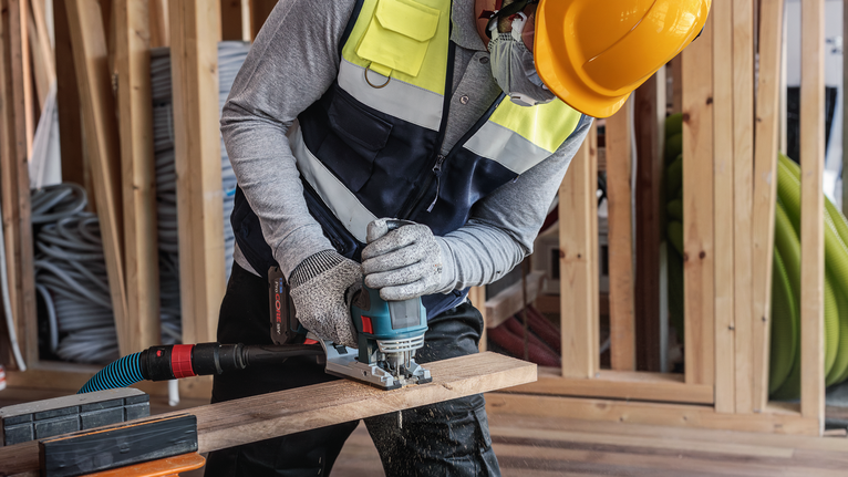 안전 장비를 착용한 사람이 건설 현장에서 전동 공구를 사용하여 나무를 자르고 있습니다.