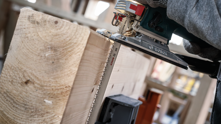 안전장비를 착용한 사람이 톱으로 두꺼운 나무 판자를 자릅니다.