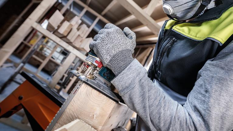 안전 장비를 착용한 사람이 톱을 사용하여 나무 들보를 자릅니다.