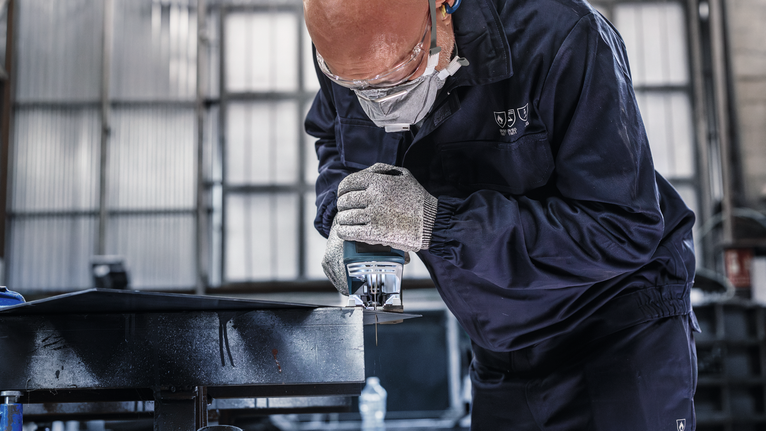 PRO Metal thick and thin T123XF 직쏘날, 100mm, 5개 안전 장비를 착용한 사람이 휴대용 전기톱을 이용해 금속을 자릅니다.