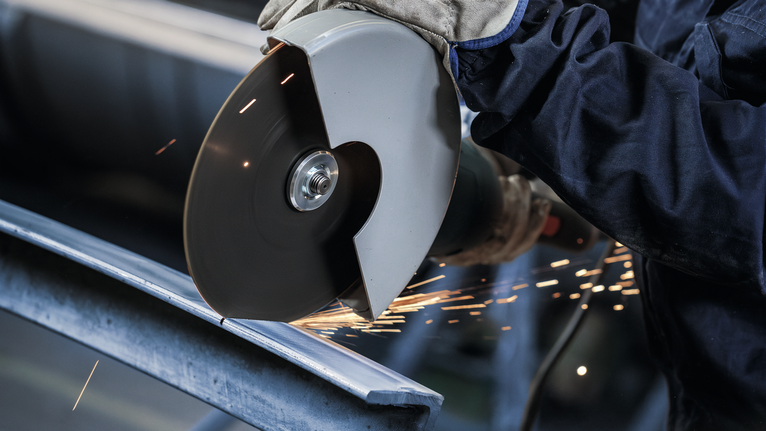 안전 장비를 착용한 사람이 각도 분쇄기로 금속을 자르는데, 불꽃이 튀네요.
