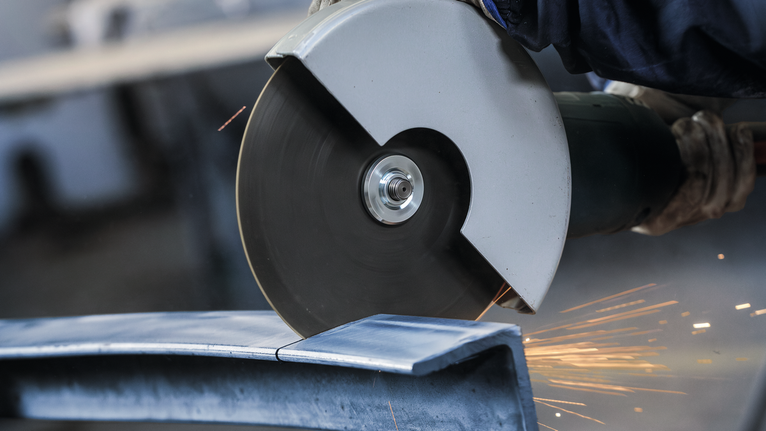 안전 장비를 착용한 사람이 대형 각도 그라인더로 금속을 자릅니다.