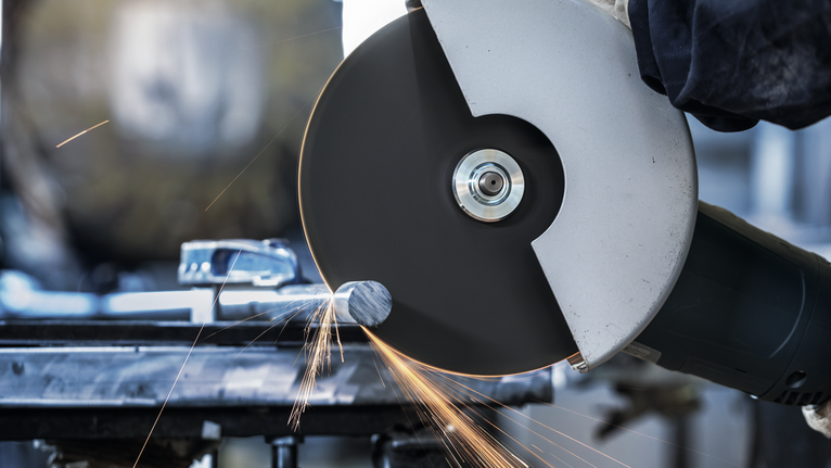 안전 장비를 착용한 사람이 불꽃을 튀기며 대형 각도 분쇄기를 사용해 금속을 자릅니다.