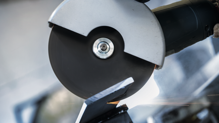 안전 장비를 착용한 사람이 각도 분쇄기를 사용하여 금속을 절단하고 있습니다.