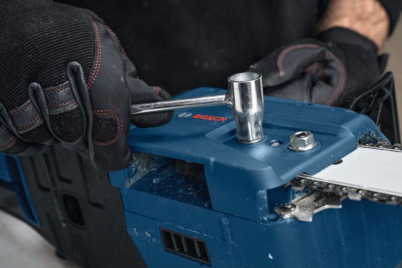 안전 장비를 착용한 사람이 렌치로 무선 전기톱을 조정하고 있습니다.