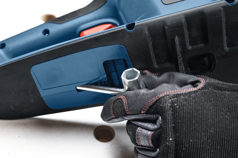 안전장비를 착용한 사람이 렌치를 사용하여 무선 전기톱을 조정하고 있습니다.