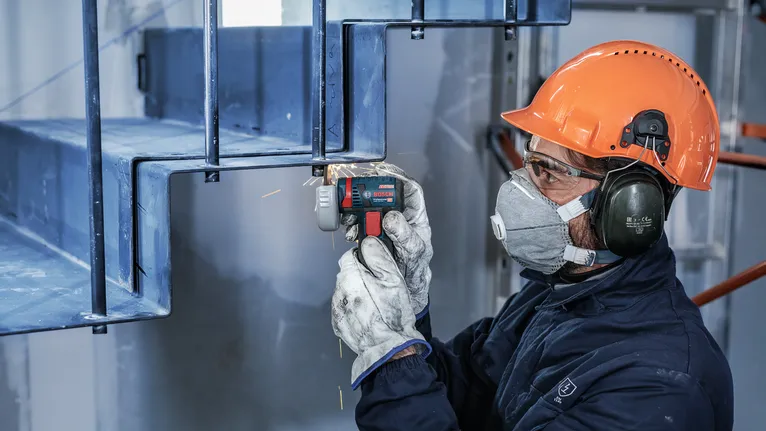 안전장비를 착용한 사람이 전동공구를 이용해 금속 계단을 갈아내고 있습니다.