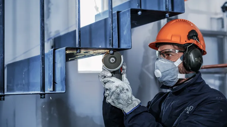 안전 장비를 착용한 사람이 금속 막대를 갈아서 불꽃을 낸다.