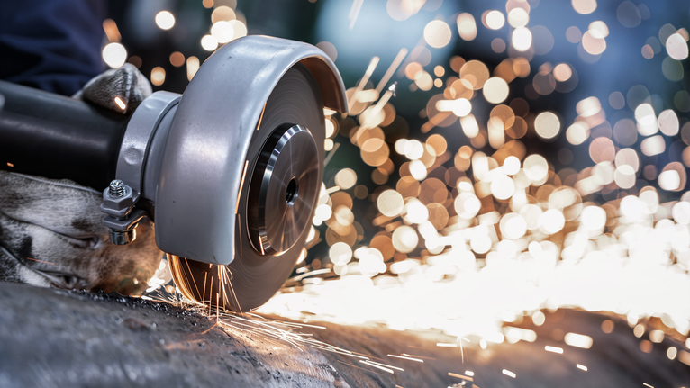 안전 장비를 착용한 사람이 각도 분쇄기를 사용하여 금속을 절단하면서 불꽃을 일으킵니다.