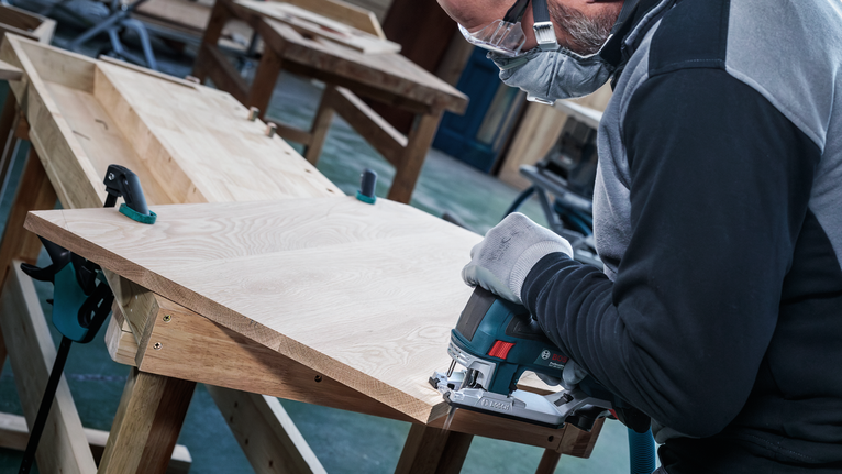 안전 장비를 착용한 사람이 퍼즐을 사용하여 나무판을 자르고 있습니다.