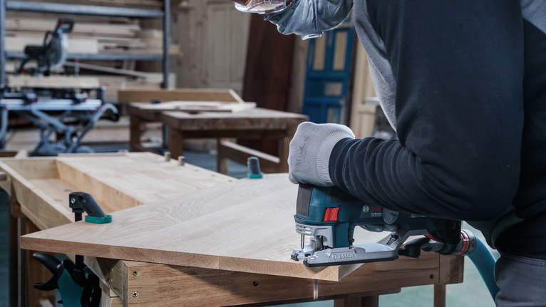 안전 장비를 착용한 사람이 작업장에서 톱으로 나무를 자르고 있습니다.