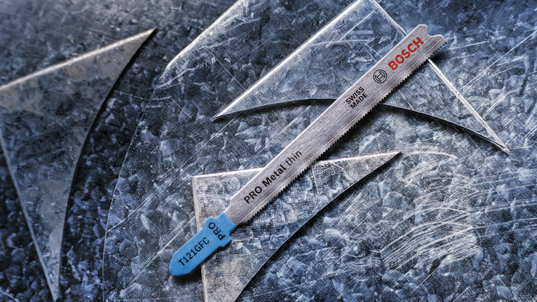 PRO Metal thin T121GFC 직쏘날, 92mm, 5개 얇은 금속을 자르는 톱날이 긁힌 금속판 위에 놓여 있습니다.