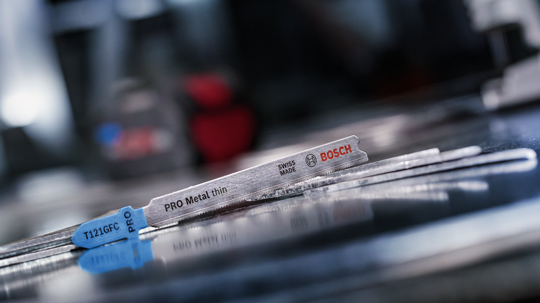 PRO Metal thin T121GFC 직쏘날, 92mm, 5개 작업장의 반사되는 금속 표면 위에 놓인 금속 톱날.