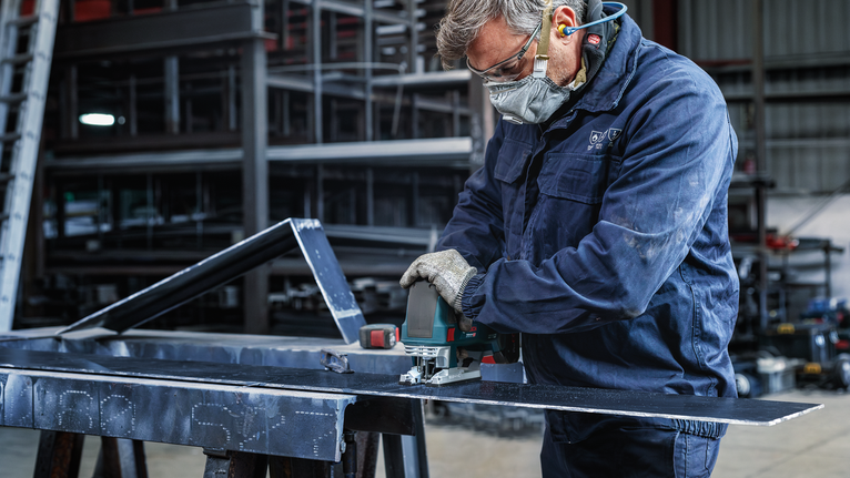 안전 장비를 착용한 사람이 전동 공구를 사용하여 금속판을 자릅니다.