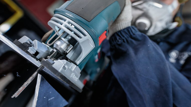 안전 장비를 착용한 사람이 퍼즐을 이용해 금속을 자르는 모습.