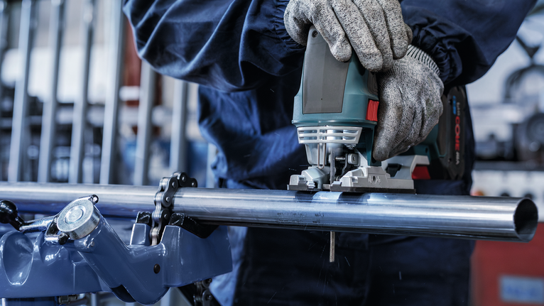 안전 장비를 착용한 사람이 퍼즐을 사용하여 금속 파이프를 자릅니다.