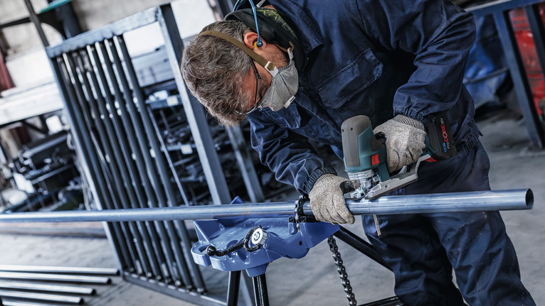 안전 장비를 착용한 사람이 산업 작업장에서 금속 파이프를 갈고 있습니다.