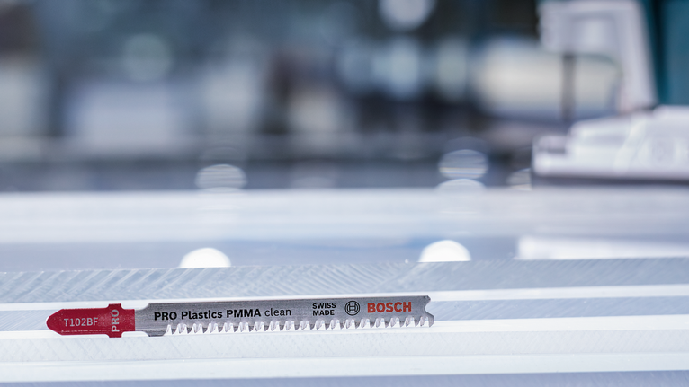 PRO Plastics PMMA clean T102BF 직쏘날, 92mm, 5개 작업장에서 투명 플라스틱 시트 위에 놓인 퍼즐 칼날입니다.