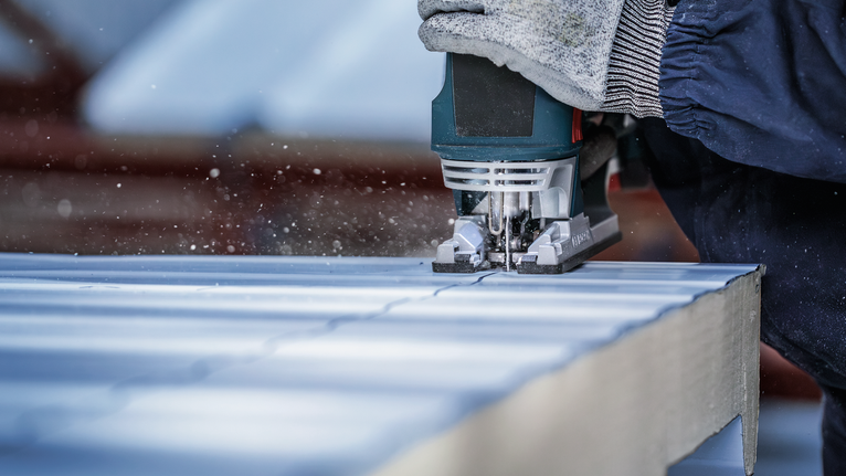 안전 장비를 착용한 사람이 톱을 사용해 패널에서 직선을 자릅니다.