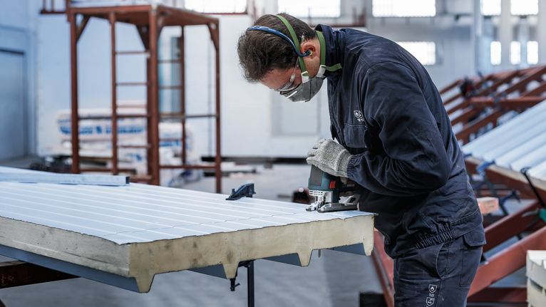 안전 장비를 착용한 사람이 전동 공구로 금속판을 자르고 있습니다.