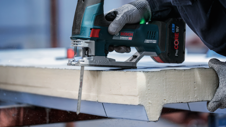 안전 장비를 착용한 사람이 무선 톱으로 폼보드를 자르고 있습니다.