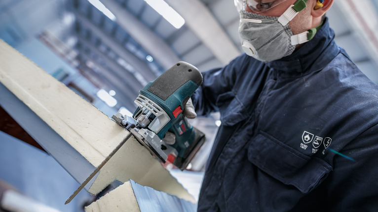 안전 장비를 착용한 사람이 전동 톱으로 폼 단열재를 자르고 있습니다.