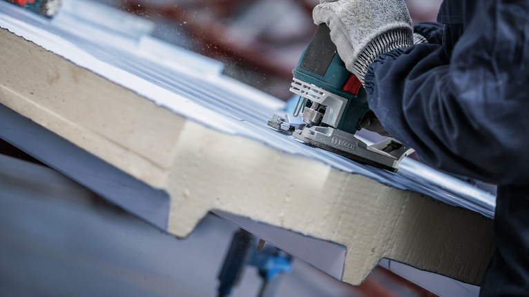 안전 장비를 착용한 사람이 톱으로 단열재를 자르고 있습니다.