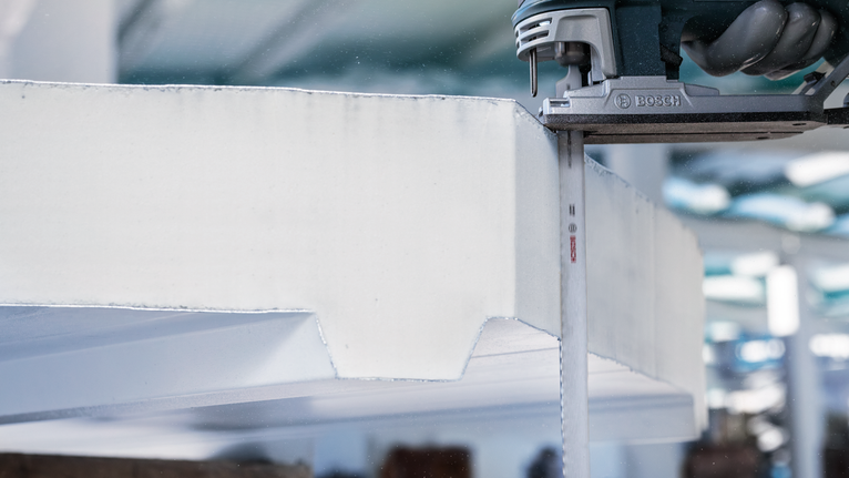 사람이 수직 왕복 톱으로 두꺼운 폼보드를 자릅니다.