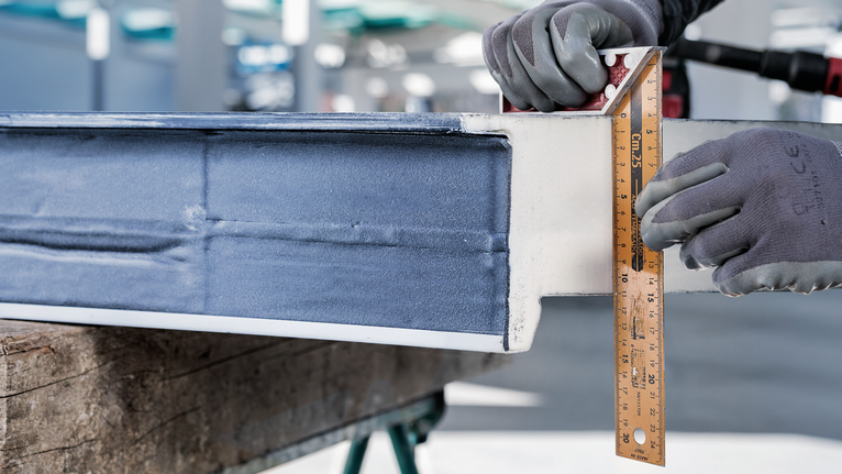 안전 장비를 착용한 사람이 자를 이용해 금속 막대를 측정합니다.