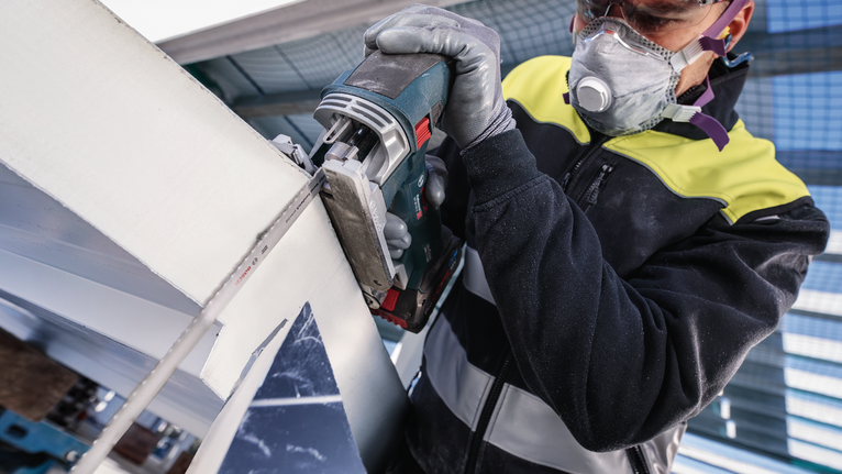 안전 장비를 착용한 사람이 전동 공구로 금속 빔을 자릅니다.